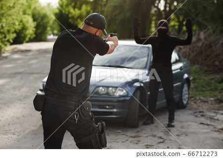 The policeman is targeting an offender near the stolen car. Stop criminality. The policeman is targeting an offender near the stolen car. Stop criminality. 66712273