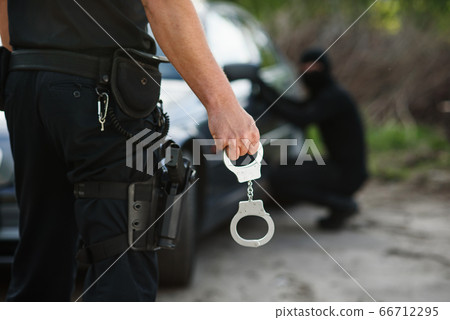 The police officer holding handcuffs in his hands. The policeman arrested the offender who stole the car. 66712295