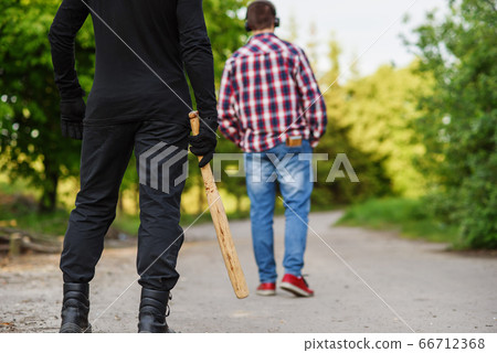 An offender in black clothes with a baseball bat in his hands attacks a man. Pickpocketing on the street during daytime. 66712368