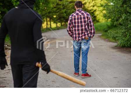 An offender in black clothes with a baseball bat in his hands attacks a man. Pickpocketing on the street during daytime. 66712372