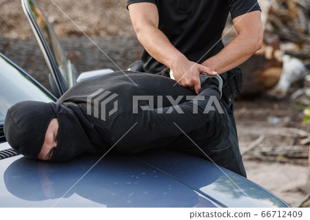 A police officer arrested the offender in a mask with a stolen car and handcuffed him on the hood of the car. 66712409