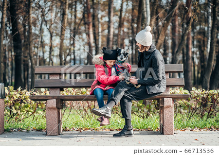 Happy mother and her daughter with dog resting on a bench Happy mother and her daughter with dog resting on a bench 66713536