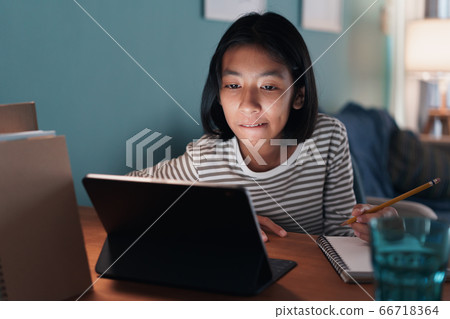 Homeschooling. Asian girl is studying online with tablet digital at desk at night Homeschooling. Asian girl is studying online with tablet digital at desk at night 66718364
