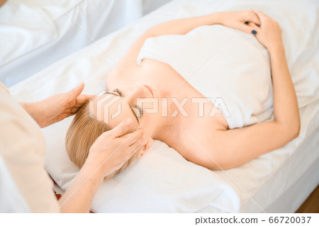 Beautiful woman receiving head and facial massage in spa salon Beautiful woman receiving head and facial massage in spa salon 66720037