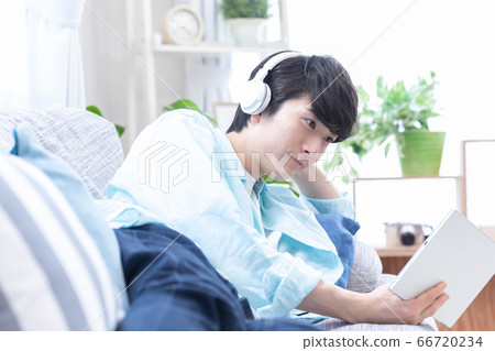 Young man wearing headphones at home and looking at tablet Young man wearing headphones at home and looking at tablet 66720234