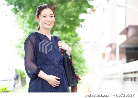 A working pregnant woman in a dress smiling at the camera A working pregnant woman in a dress smiling at the camera 66726537