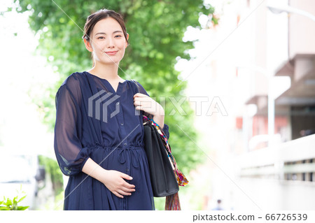 A working pregnant woman in a dress smiling at the camera A working pregnant woman in a dress smiling at the camera 66726539
