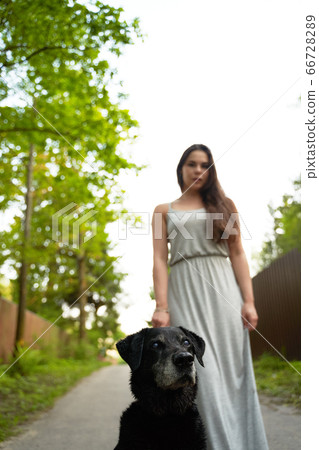Brunette on walk with black dog in park on summer day. Brunette on walk with black dog in park on summer day. 66728289