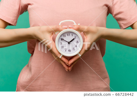 Woman holding alarm clock in hand on blue Woman holding alarm clock in hand on blue 66728442