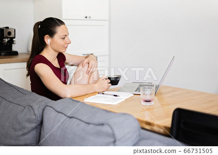 Millennial woman works from home. Kitchen room with wooden table and coffee cup. E-learning 66731505