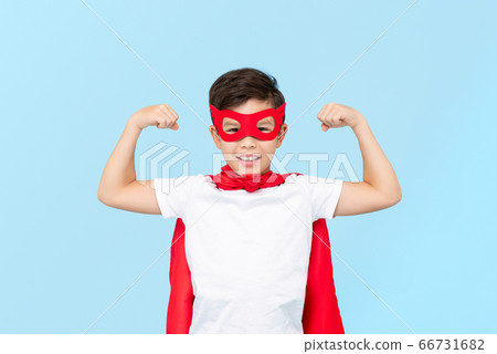 Cute superhero boy in red mask and cape flexing arm muscles 66731682