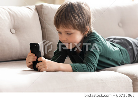 Cute little boy using smartphone, lying on cozy couch 66733065