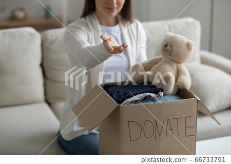 Woman with arm stretched sit near donation box with clothes 66733791