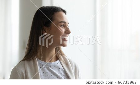 Happy young woman standing near window looking in distance smiling Happy young woman standing near window looking in distance smiling 66733962