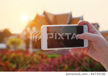 Woman's hand takes pictures on phone Wat Ratchanatdaram temple in Bangkok at sunset, Thailand Woman's hand takes pictures on phone Wat Ratchanatdaram temple in Bangkok at sunset, Thailand 66734190
