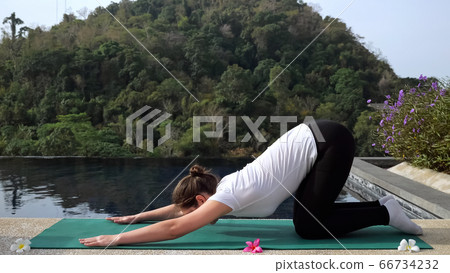 Young woman in fitness uniform doing stretching near the pool outdoors 66734232