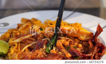 Someone is eating Thai noodles with chopsticks 66734279