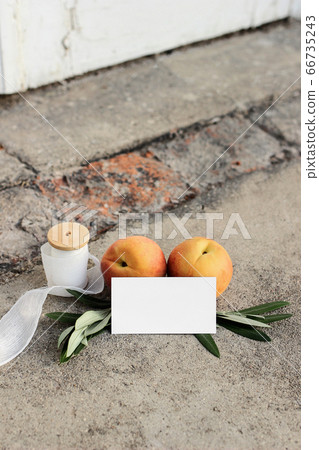 Summer wedding still life scene. Blank business card, invitation mock-up. Olive branches, silk ribbon and peaches fruit on grunge concrete background. Blurred old white door. No people, vertical 66735243