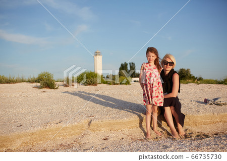 Smiling mother and beautiful daughter having fun on the beach. Portrait of happy woman giving a piggyback ride to cute little girl with copy space. Portrait of kid embracing her mom during summer. Smiling mother and beautiful daughter having fun on the beach. Portrait of happy woman giving a piggyback ride to cute little girl with copy space. Portrait of kid embracing her mom during summer. 66735730