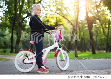 Cute adorable beautiful caucasian little blond girl enjoy riding white small bicycle by path in green summer city park forest or garden at bright sunny day outdoor. Children healthy lifestyle concept 66737728