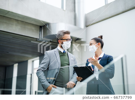 Flight attendant talking to businessman on airport, wearing face masks. 66737799