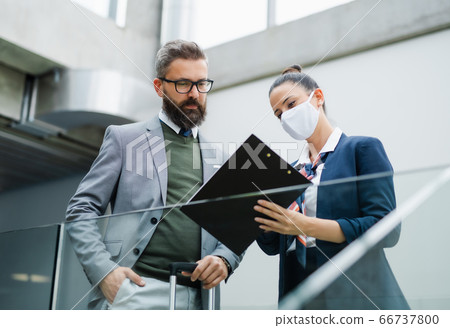 Flight attendant talking to unrecognizable businessman on airport, wearing face masks. 66737800