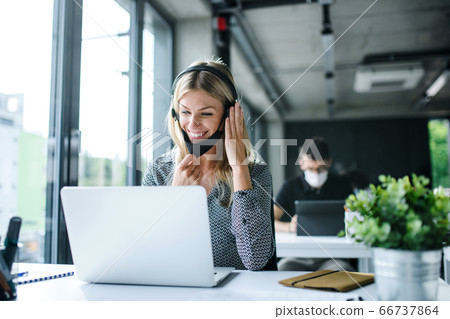 Young woman with face mask and headphones back at work in office after lockdown. Young woman with face mask and headphones back at work in office after lockdown. 66737864