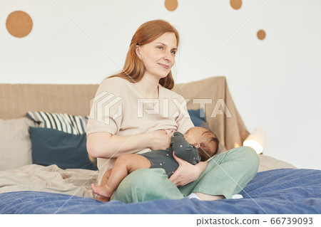Mature Mother Breastfeeding Baby on Bed 66739093