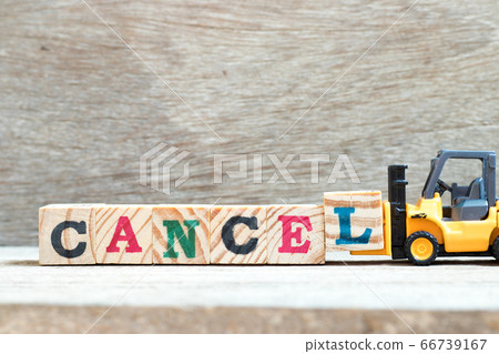 Toy forklift hold letter block L to complete word cancel on wood background 66739167
