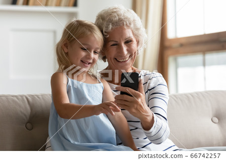 Little granddaughter aged grandmother having fun at home using smartphone 66742257