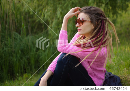 Outdoors portrait of a girl with dreadlocks wearing pink sweater and sunglasses in a city park during a sunset, be free concept. Outdoors portrait of a girl with dreadlocks wearing pink sweater and sunglasses in a city park during a sunset, be free concept. 66742424