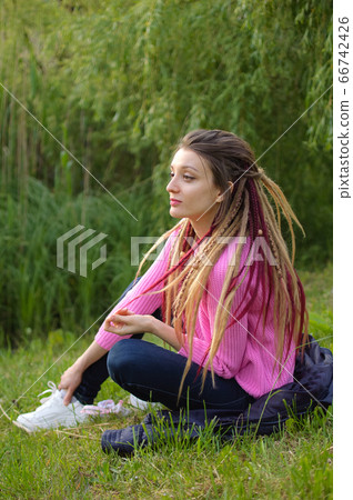 Outdoors female portrait of a modern girl with dreadlocks wearing pink sweater and dark jeans in a city park during a sunset, be free, be youself concept Outdoors female portrait of a modern girl with dreadlocks wearing pink sweater and dark jeans in a city park during a sunset, be free, be youself concept 66742426