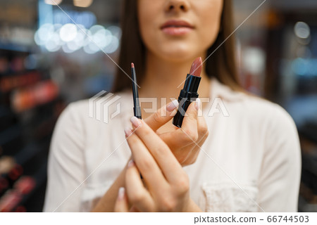 Woman shows lipstick and liner in cosmetics store Woman shows lipstick and liner in cosmetics store 66744503