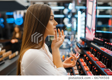 Woman applies lipstick in cosmetics store Woman applies lipstick in cosmetics store 66744508