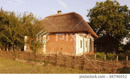 Old east european rural wooden house with wattle fence and thatched roof. 66746052