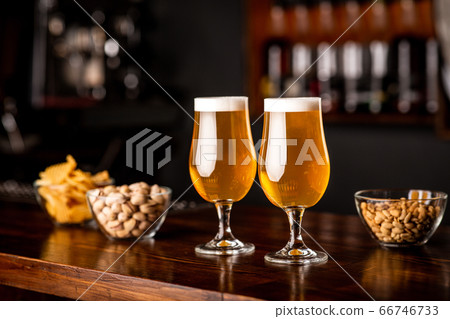 Snacks in pub on wooden bar. Two glasses with beer, chips, nuts and pistachios 66746733