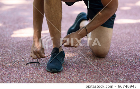Young sportsman tying shoelaces during his morning run outdoors, close up of legs Young sportsman tying shoelaces during his morning run outdoors, close up of legs 66746945