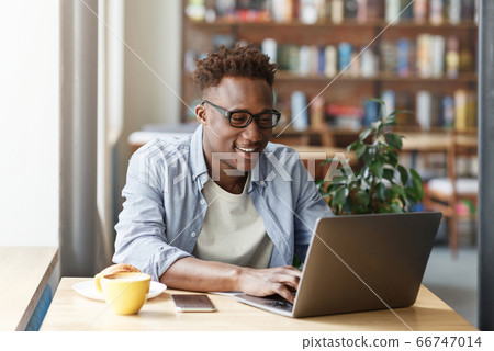 Joyful African American student doing his online homework at urban cafe Joyful African American student doing his online homework at urban cafe 66747014