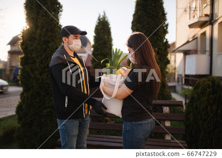 Courier in protective mask and medical gloves delivers fresh food for female customer. Delivery service under quarantine. Coronavirus covid-19 theme 66747229