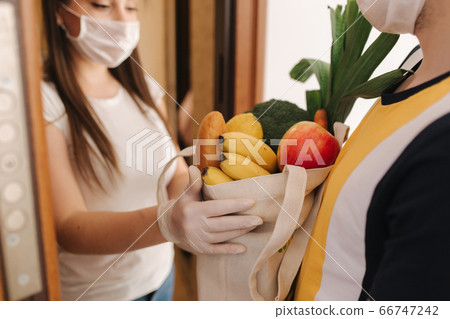 Delivery man in mask and gloves give fresh food to recipient and young woman customer. Stay home, Online shopping concept Delivery man in mask and gloves give fresh food to recipient and young woman customer. Stay home, Online shopping concept 66747242