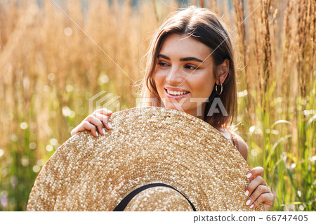 Beautiful smiling woman holding straw hat in hands standing outdoors 66747405