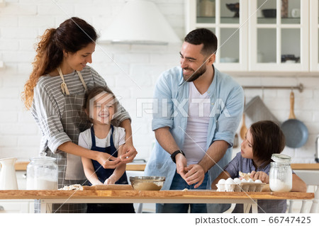 Caring father and mother playfully teaching little children to cooking. Caring father and mother playfully teaching little children to cooking. 66747425