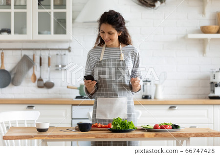 Happy young attractive woman cooking to recipe on smartphone. Happy young attractive woman cooking to recipe on smartphone. 66747428