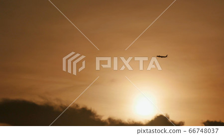 Take off the plane in the distance against the background of sunrise or sunset. Silhouette of an airplane. Airplane in the sky at sunset. Take off the plane in the distance against the background of sunrise or sunset. Silhouette of an airplane. Airplane in the sky at sunset. 66748037