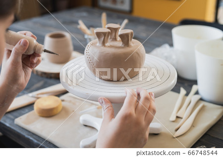 Closeup of bottom of mug, which is being decorated in ceramic studio. Female professional hands making clay dots or drops on the surface of vase by special squeezing tool. 66748544