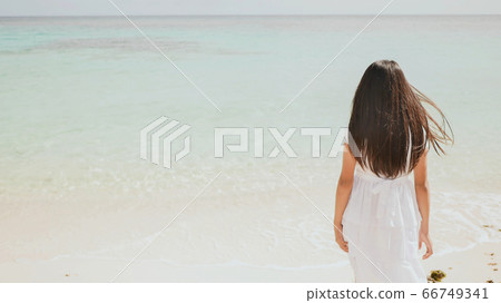 A charming philippine schoolgirl in a white dress is walking along a white sandy beach. Enjoying the tropical scenery. Childhood. 66749341