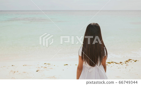 A charming philippine schoolgirl in a white dress is walking along a white sandy beach. Enjoying the tropical scenery. Childhood. 66749344