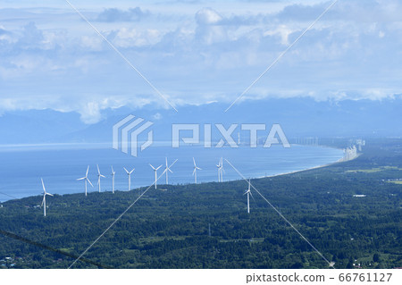 A landscape with many white windmills on the hill overlooking the blue-lined bay 66761127
