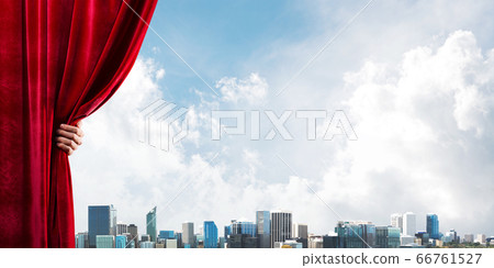 Business city behind red curtain and hand holding it Business city behind red curtain and hand holding it 66761527
