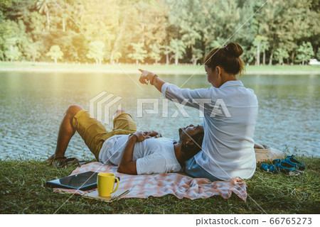 Asian couple lover sitting a relax River side in the public park. working with a notebook Asian couple lover sitting a relax River side in the public park. working with a notebook 66765273